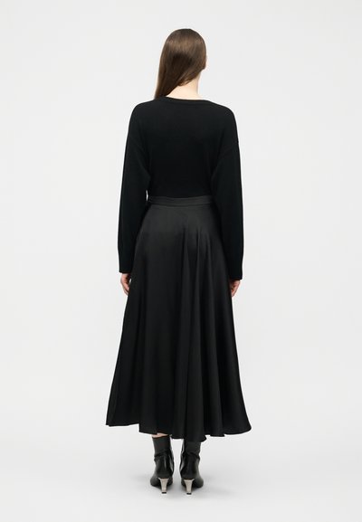 Kobieta stojąca tyłem, ubrana w czarny sweter z długim rękawem, czarną spódnicę do połowy łydki i czarne botki na obcasie.