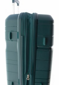 Hardshell koffer in donkergroen met een gestructureerd oppervlak, dubbele ritssluiting, bovenhandvat en zijklemmen voor gemakkelijk hanteren.