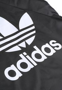Textil negro con un gran logo blanco de Adidas que presenta tres rayas y un diseño gráfico de hoja. Textura suave, diseño minimalista.