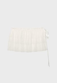Demi-tabliers en dentelle blanche avec ceinture froncée et long ruban latéral sur fond gris.