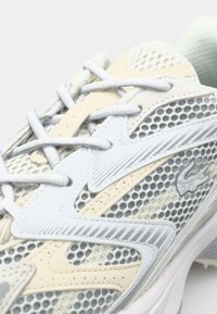 Heledat hall spordijalats võrkmustriga, tekstuursete pealiskihiga, beežide aksentidega ja valgete paeltega. Küljel on brändi embleem.