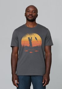 Grijze katoenen T-shirt met een oranje zonsondergangafbeelding van een visser met vissen, weergegeven in een rond ontwerp boven een lijn van kleinere vissen.