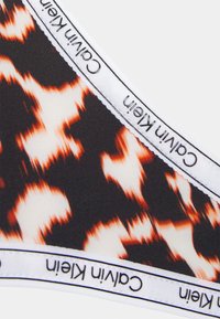 Boxers Calvin Klein com um padrão abstrato em preto, branco e laranja, com uma banda elástica branca exibindo o nome e o logotipo da marca.