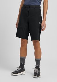 Schwarze Outdoor-Shorts mit figurbetontem Design, aus einem strapazierfähigen Material gefertigt. Verfügt über einen Frontknopfverschluss und Seitentaschen. Getragen mit grauen Socken im Bergmuster.