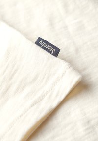 Hvidt stof foldet med et lille navyblåt mærke med brandnavnet syet ind i sømmen.