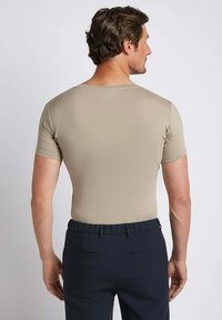 Man facing away wearing a fitted beige short-sleeve shirt and black trousers against a plain light background.