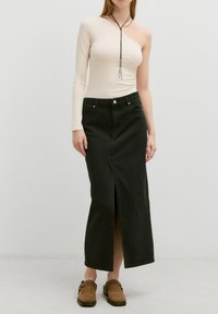 Zwarte denim maxi rok met een voorklep, gecombineerd met een beige langemouwtop met een enkele schouderontwerp. Bruine instapklompen.