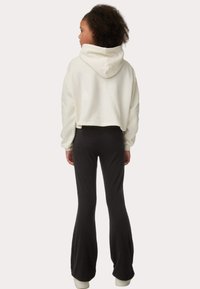 Weißer, verkürzter Hoodie mit Kapuze und langen Ärmeln, kombiniert mit schwarzen, ausgestellten Leggings. Weicher Stoff mit minimalistischem Design.