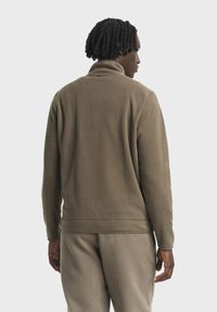 Olivgrüner Fleece-Pullover mit hohem Kragen, weicher Textur und figurbetontem Design. Mit einer Nahtdetails an der Taille und den Bündchen.