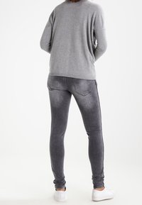 Pull gris associé à un jean skinny gris foncé. Le jean présente une texture lisse et des poches, complétés par des baskets blanches.