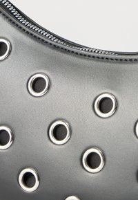 Κοντινό πλάνο τμήματος γκρι δερμάτινης τσάντας με ασημένια μεταλλικά ροδέλες και εμφανές κυρτό φερμουάρ κατά μήκος της πάνω άκρης.