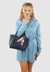 Marineblauwe leren tote bag met dubbele handgrepen, voorzien van een decoratieve sjaal in contrasterende kleuren. Gladde textuur met metallic accenten aan de onderkant.