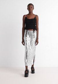Haut court noir texturé avec des fines bretelles, associé à une jupe maxi en sequins argentés avec une fente sur le côté, et des chaussures à plateforme noires chunky.