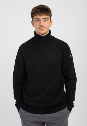 Maglione nero a collo alto con polsini e orlo a coste, dotato di maniche raglan e un piccolo dettaglio logo sul braccio sinistro. Texture liscia.