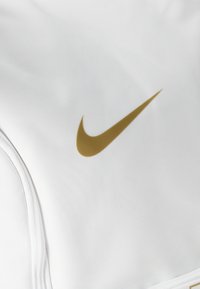 Biela športová tkanina s textúrovaným povrchom, na ľavej strane so zvýrazneným zlatým logom Nike swoosh. Štíhle, hladké švy.