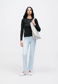 Čierne tričko s dlhými rukávmi s bielym logom, svetlomodré nohavice a biele tenisky. Modelka nesie svetlosivú tašku na rameno.