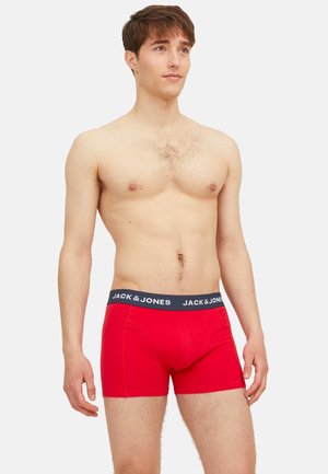 Red cotton boxer shorts with a black waistband featuring "JACK & JONES" logo. Smooth texture, fitted design. Model shown is shirtless.