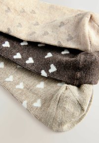 Tre paia di calzini in tonalità beige e marrone con diversi piccoli motivi a cuore bianco. Tessuto a maglia testurizzato con una finitura liscia.