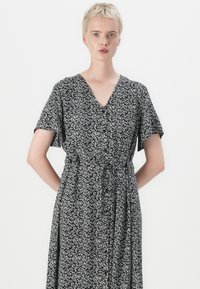 Vestido floral em preto e branco com mangas curtas, decote em V e cintura priseada. O tecido parece leve com uma textura suave.