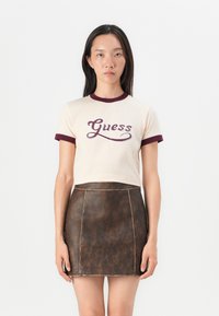 Kremfarget kortermet t-skjorte med marsalrød ribbet krage og mansjetter, med "Guess" logo i mørk marsalrød, kombinert med et brunt lærskjørt.