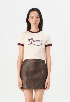 Grietai trumpomis rankovėmis marškiniai su bordo spalvos rauktomis apykaklėmis ir rankogaliais, ant kurių yra "Guess" logotipas tamsiai bordo spalvos, derinami su ruda odine sijonu.