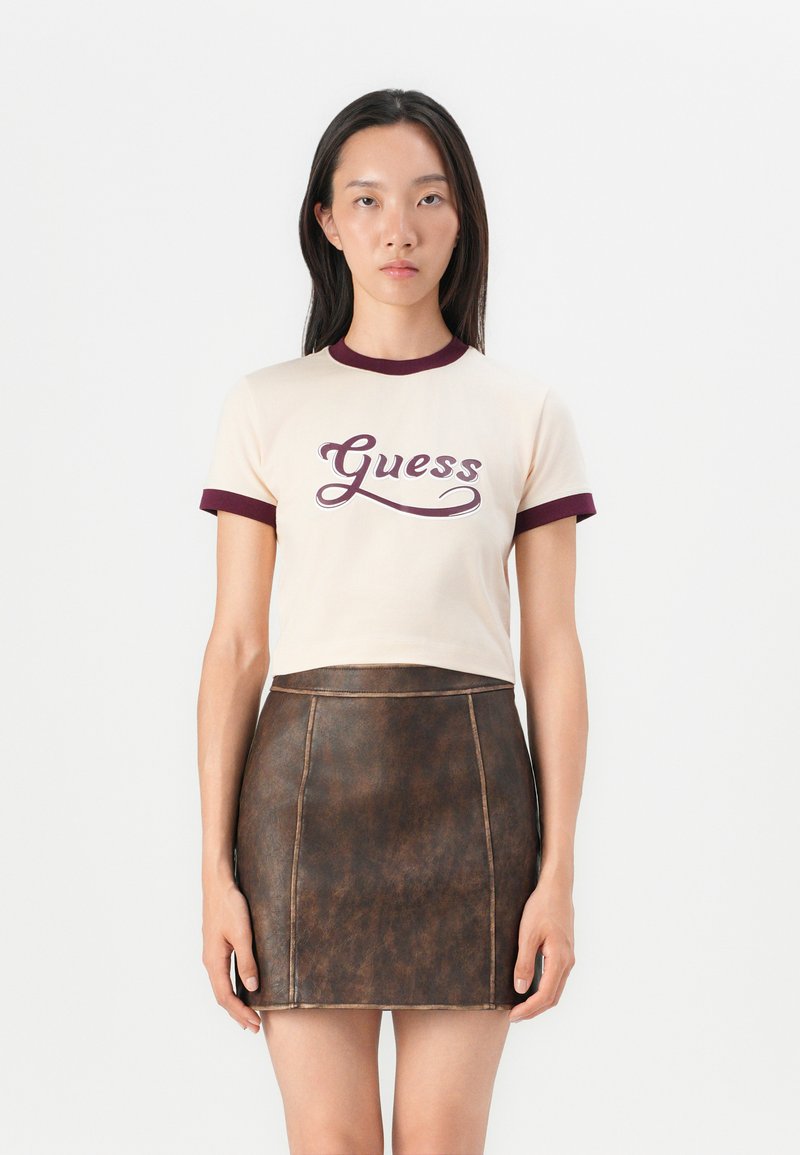 Kremfarget kortermet t-skjorte med marsalrød ribbet krage og mansjetter, med "Guess" logo i mørk marsalrød, kombinert med et brunt lærskjørt.