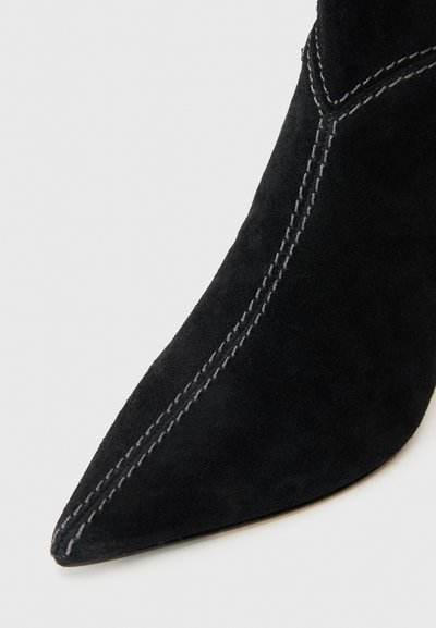 Schwarze Ankle Boots aus Wildleder mit spitz zulaufender Zehenpartie, kontrastierenden grauen Nähten entlang der Nähte und einer glatten Sohle.