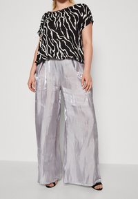Top a righe zebrate in bianco e nero con maniche corte, abbinato a pantaloni larghi in argento chiaro lucido e sandali neri con punta aperta.