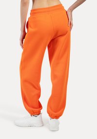 Orange Sweatpants aus weichem Material, mit geripptem Taillenbund und elastischen Bündchen, kombiniert mit weißen Freizeitsneakern.