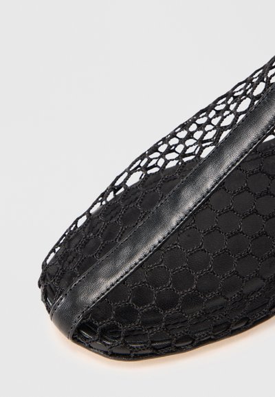 Scarpa nera con tomaia in mesh e dettagli in pelle, che mostra un primo piano del motivo tessuto a rete aperta e l'accento in pelle liscia.