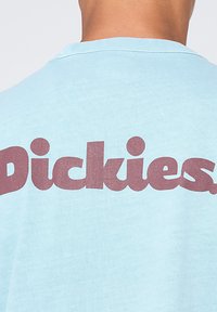 Camiseta azul claro con texto burdeos oscuro que dice "Dickies" en la parte de atrás, hecha de una tela suave con un corte relajado.