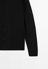 Zwarte gebreide cardigan met knopen aan de voorkant, een geribbelde textuur, lange mouwen en een enkele opgestikte zak aan de onderzijde van de linkerzijde.