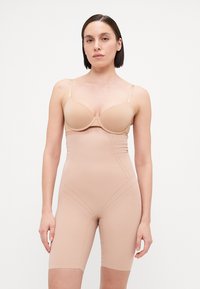 Nude oblikovalna bodysuit z gladko teksturo, strukturirano zasnovo in kratkimi nogami, z nastavljivimi naramnicami in brezšivnimi robovi.