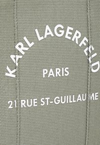 Šedá textúrovaná tkanina s bielym potlačeným textom: "KARL LAGERFELD," "PARÍŽ," a "21 RUE ST-GUILLAUME," usporiadaný do polkruhu.
