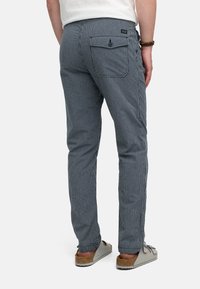 Pantalons rayés pour hommes en bleu marine et blanc, avec une coupe slim, une poche arrière avec fermeture à bouton, et un tissu doux et texturé.