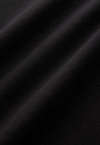 Gros plan sur un tissu noir texturé avec un motif en forme de grille et des plis doux créant des ombres douces.
