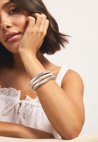 Silver textured bangles stacked on a wrist, featuring a wavy pattern, worn by a person with a light skin tone and short hair.