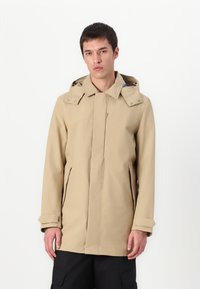 Beige yderjakke med hætte, frontlukning med lynlås, to sidelommer og et rent, minimalistisk design. Glat tekstur og let materiale.