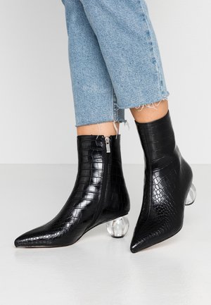 Stivaletti alla caviglia in pelle nera con texture coccodrillo, punte appuntite e tacchi tondi trasparenti, indossati con jeans di jeans azzurri cropped.