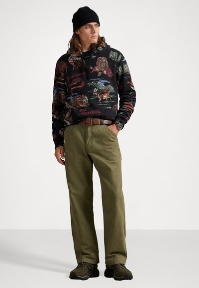 Felpa nera con grafiche colorate a tema outdoor, pantaloni verde oliva, berretto nero e scarpe sportive scure. Motivi dettagliati sulla felpa.