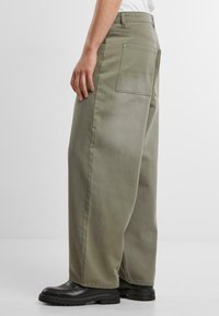 Light green wide-leg pants made of cotton blend fabric; features two back pockets and subtle texture. Paired with black footwear.