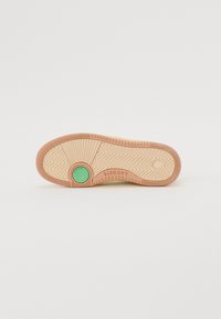 Suola della scarpa con fondo in gomma testurizzata di un beige chiaro, con un accento circolare verde sul tallone e un motivo a zigzag per una migliore aderenza.