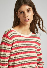 Maglione lavorato a maglia con righe rosse, crema e olive, caratterizzato da un collo rotondo e un tessuto texturizzato. Maniche lunghe con dettagli ai polsini.