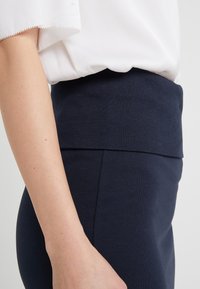 Rekbare marineblauwe broek met een brede geribde tailleband, gemaakt van een zachte stof. Zichtbare naaddetails en een gladde textuur.