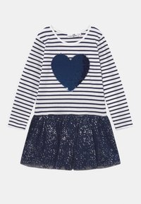 Randig långärmad klänning med ett marinblått paljett hjärta på vit botten, accentuerad av en plisserad marinblå tyllkjol med silverglittriga detaljer.