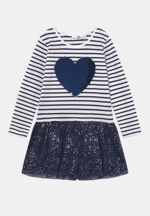 Raidallinen pitkähiha dressi, jossa on tummansininen paljettisydän valkoisella pohjalla. Mekon alaosa on akryylinen tummansinisestä kangastosta valmistetusta laskostetusta tyllihameesta, jossa on hopeanvärisiä kimalteleita.