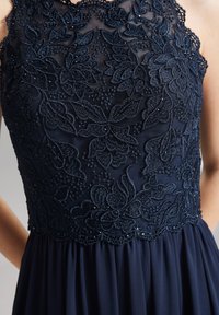Marineblaues Kleid mit aufwendiger floralem Spitzenstickerei am Oberteil, verziert mit Perlen, und einem fließenden, gefältelten Rock.