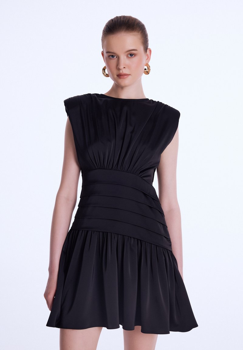 Robe noire sans manches avec bodice froncé, texture plissée et jupe évasée. Présente un tissu lisse et un design de taille structuré.
