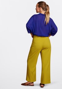Blauwe doorschijnende blouse met een losse pasvorm, gecombineerd met gele hoge taille broeken met wijde pijpen. Bruine flats met dierenprint maken de outfit af.