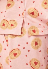 Tissu rose imprimé de motifs de biscuits avec des cœurs et de petits cœurs rouges dispersés, avec une texture douce et lisse.
